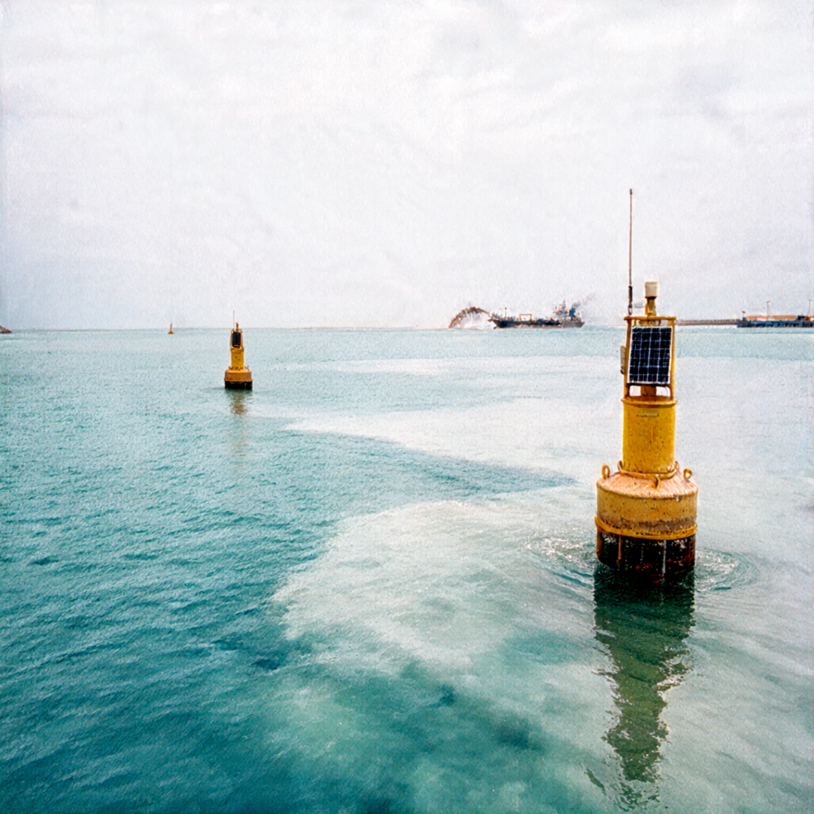 Yellow buoys on the water, with a solar panel and antenna on the nearest buoy, pale streaks across the water and a vessel in the distance.