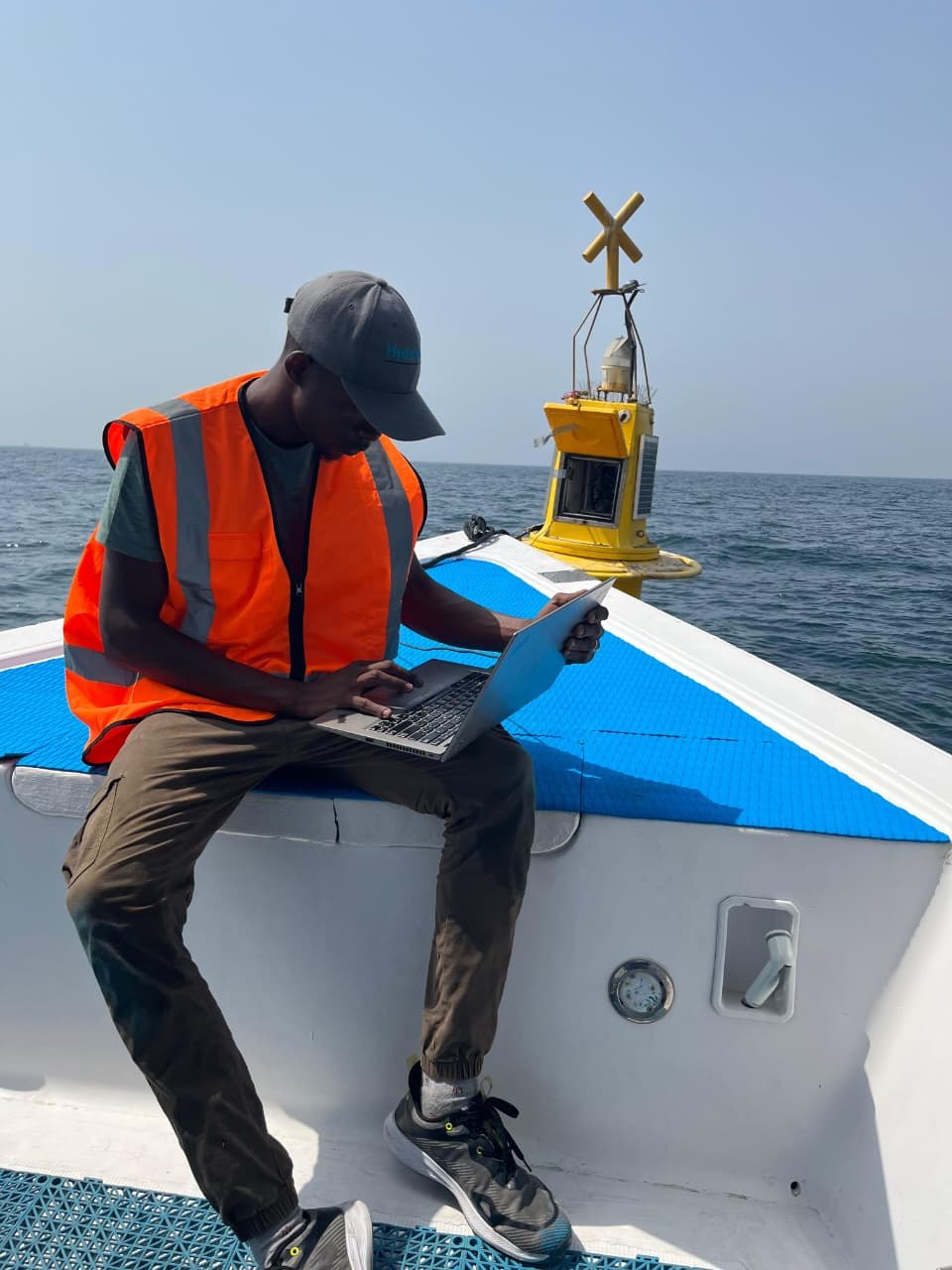 Husam using a laptop on a boat with a Fujairah monitoring buoy behind him