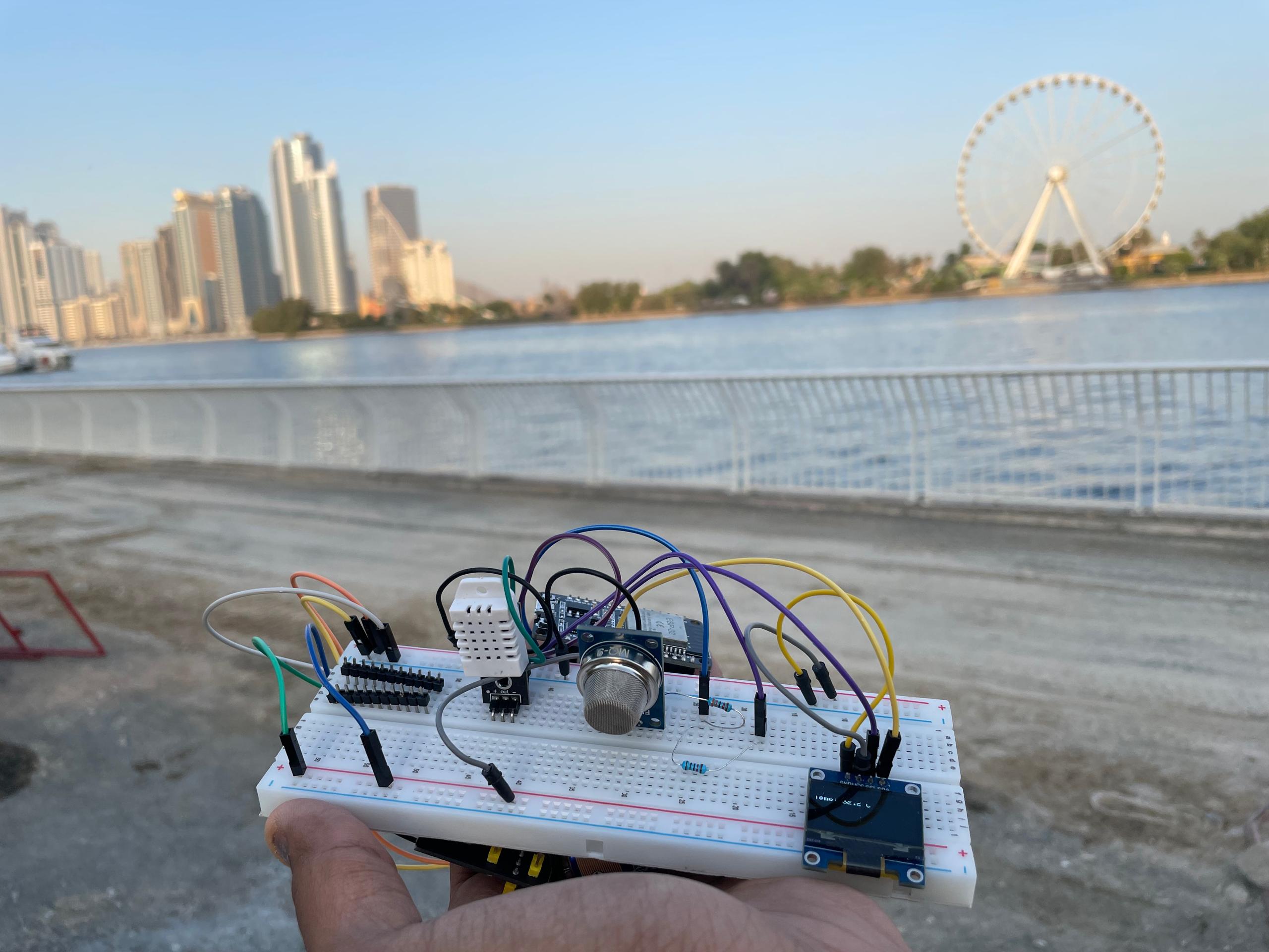 Hand holding the ESP32 breadboard experiment outdoors beside a waterfront